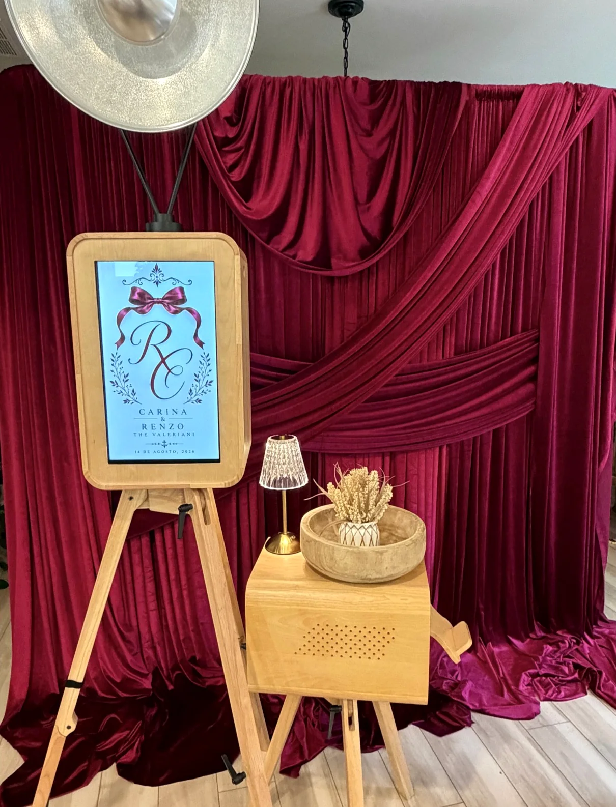 Photo booth with a monogram screen in front of burgundy velvet drapery
