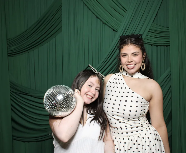 Two guests with a disco ball in front of emerald drapery