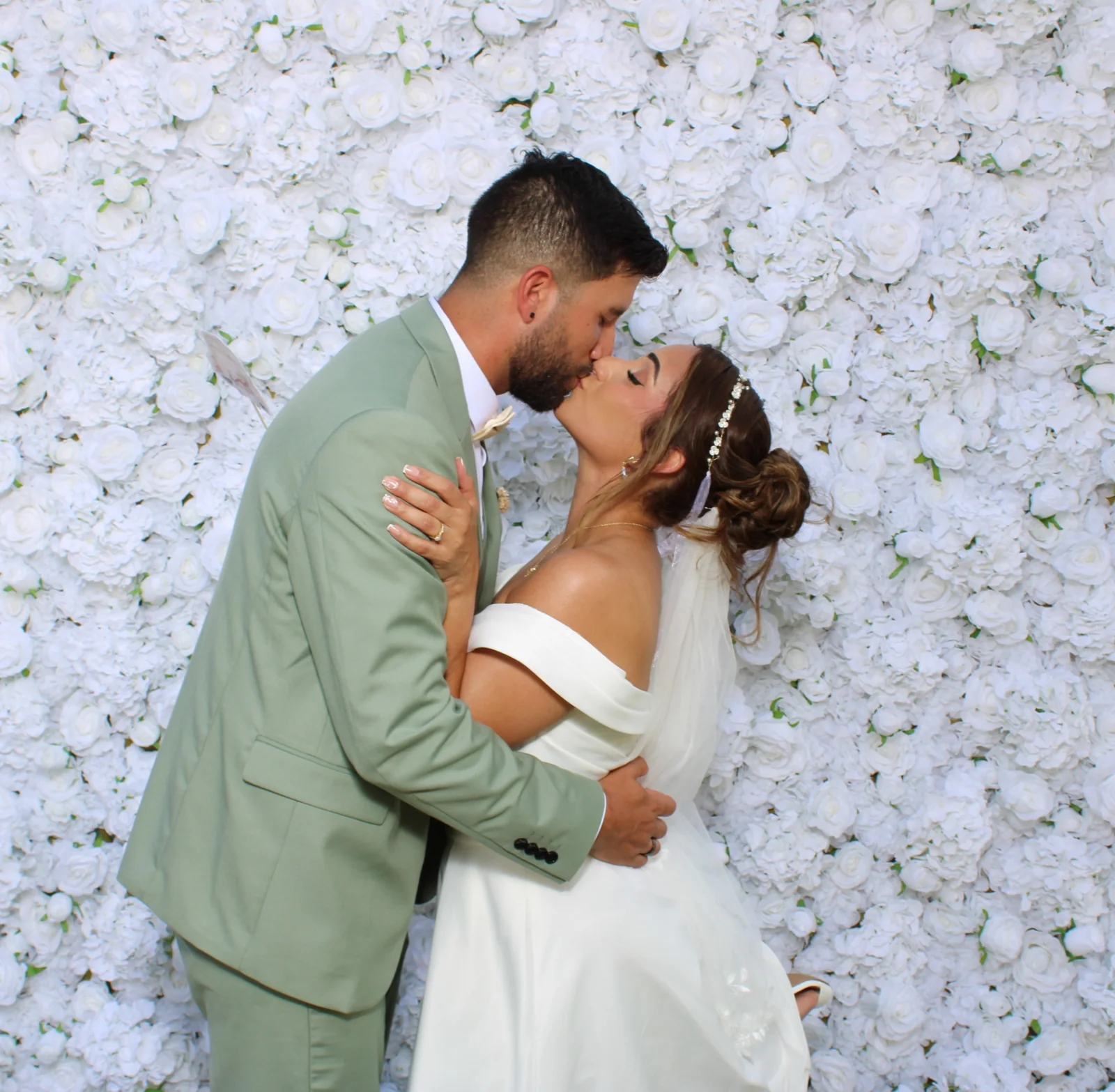 Bride and groom kissing in front of the Luxury Memories white flower wall