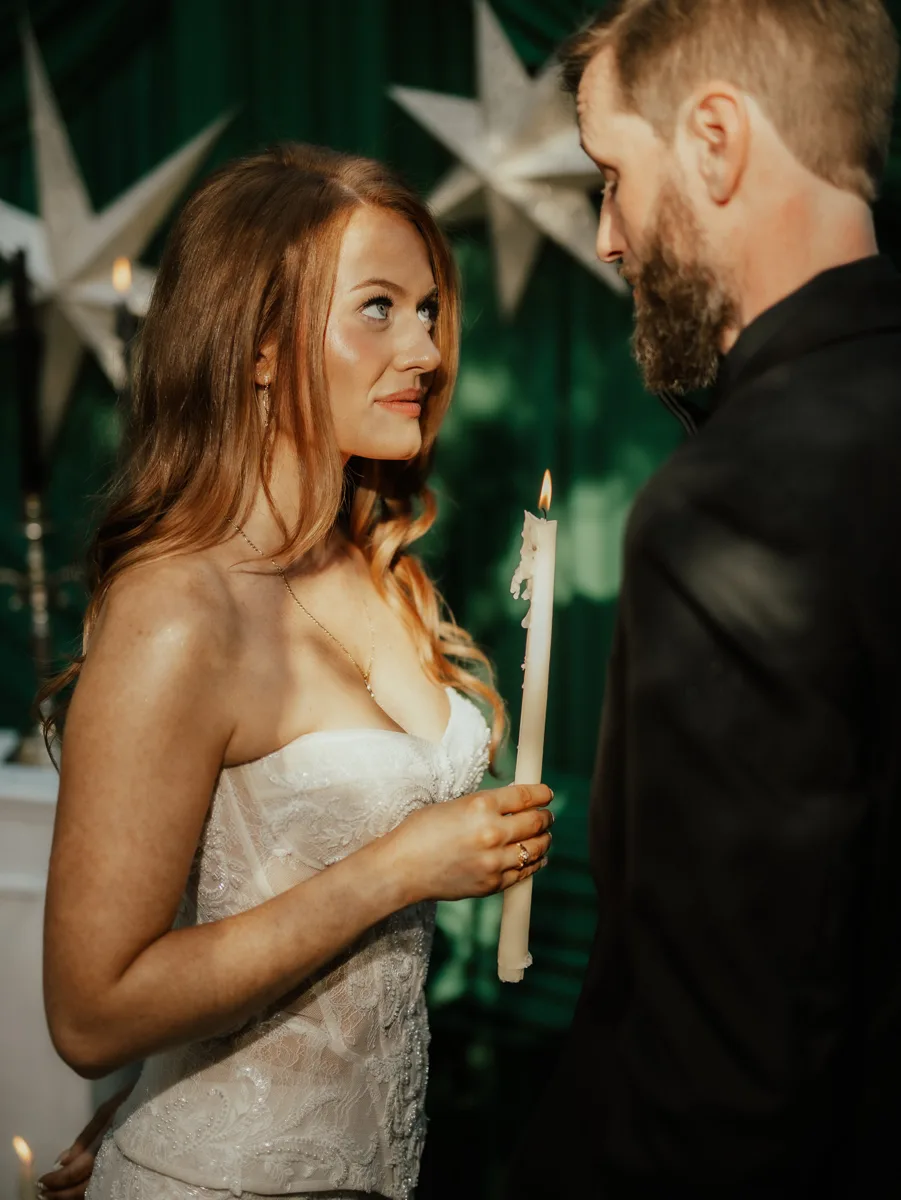 Bride holding a candle and gazing at the groom in front of emerald drapery and paper stars